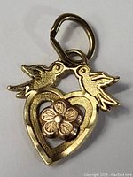 Front close-up image of 14K gold pendant charm showing two love birds, an open heart shape, and a central flower detail.