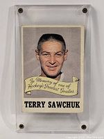 Front view of the Terry Sawchuk hockey card inside a clear plastic screw-down case showing the portrait and commemorative banner.