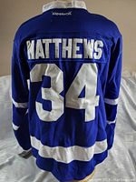 Back of blue hockey jersey showing "MATTHEWS 34" with Reebok branding at collar