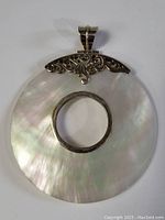 Front view of large circular mother of pearl pendant with sterling silver decorative top and circular ring centerpiece.