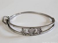 Sterling silver bangle bracelet showing the three maple leaf emblems and safety chain.