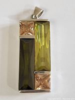 Front view of rectangular sterling silver pendant with three faceted gemstones in green and peach tones including a large olive green rectangular stone and two square peach stones.