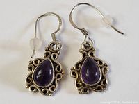 Pair of sterling silver earrings with teardrop shaped amethyst stones surrounded by ornate art nouveau inspired silver scrollwork.