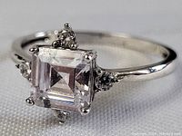 Close-up detail of the front of the sterling silver ring showing the square-cut clear center stone and four accent stones.