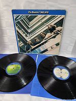 Open double vinyl album with two black records visible and portion of blue inner sleeve. Apple record labels on both discs.