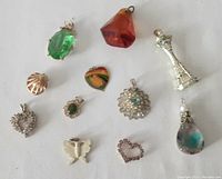 View of all 11 pendants in a single image showing the different shapes and colors including green gemstone, amber stone, chess piece, shell, hearts, butterfly, floral, and a teardrop pendant.