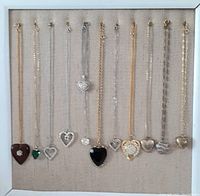 Twelve heart-shaped necklaces displayed on fabric backing. Variety of pendant designs and chain types visible.