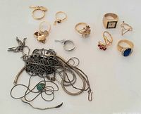 Overall view of gold-tone rings arranged above a tangle of silver-tone chains and pendants