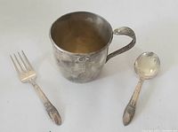 Child's cup, spoon, and fork shown together to display the full set