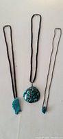Three necklaces laid flat on a light surface. Includes a large turquoise chip dome pendant on a black heishi bead strand with silver findings, a smaller turquoise chip pendant necklace with black heishi beads, and a small turquoise stone on a thin light-colored cord.