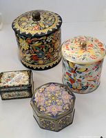 Four decorative tin containers in a group showing their different shapes and colorful floral designs
