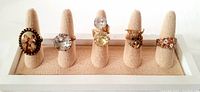 Full view of five rings lined up on a beige ring display holder showing variety of designs and sizes.