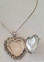 Close-up of the open heart-shaped silver locket showing the smooth interior and detailed filigree floral border around the edge.