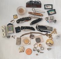 Photo showing variety of vintage coins, rings, folding knives, pins, dice, vintage lighters, pocket watch, collectible motorcycle figurine and other small items