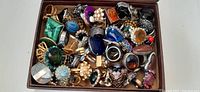 Jewelry box filled with an assortment of decorative rings featuring different stones, metals, and styles.