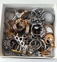 Top-down photo of the lot showing a mix of rings in different metals and styles piled in a box.
