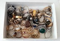 Top-down photo of box filled with assorted rings showing mixed metals and stones.