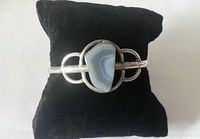 Front view of sterling silver cuff bracelet with central polished agate stone on black cushion.