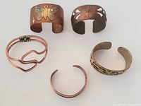 Lot of 5 vintage copper bracelets arranged in two rows showing varied designs and conditions.