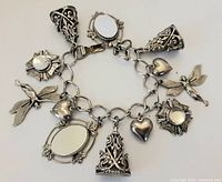 Photo showing the full layout of the vintage silver tone charm bracelet with detailed charms including mirrors, hearts, fairies, and ornate elements.