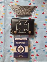 Photo showing Aerosmith belt buckle, black wallet with white cross, and Winnipeg Jets playing cards.