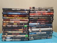Stack of 39 DVD cases of various horror and thriller movie titles arranged in two piles.