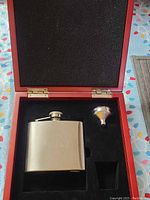 Photo of open wooden box containing stainless steel flask and funnel in foam inserts.