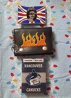 Top view of all three items laid out on a patterned fabric: belt buckle, flame wallet, and Vancouver Canucks playing cards.