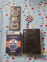 Full lot view showing playing cards box, keychain bottle opener in packaging, shaped key, and black wallet on a colorful cloth background.