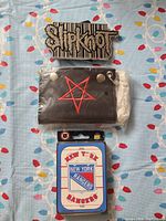 Front view of the Slipknot belt buckle, wallet showing red star, and New York Rangers playing cards.