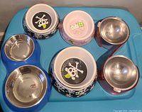 Top view of all three pet bowls including two raised bowls with pink stands and blue stand with stainless steel dishes and two individual bowls with cartoons and skull designs