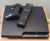 Sony PlayStation 3 console with wired controller and remote control on top.
