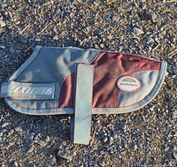 Top side view of WeatherBeeta dog coat laid flat showing maroon and grey fabric and reflective strip on the side flap.