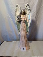 Front view of wooden angel figurine showing pink dress, bells, and large white wings with distressed paint.