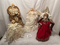 Image showing 4 angels including one in white satin dress, one in velvet red gown, one with gold wings holding a dove, and one angel with floral wreath.