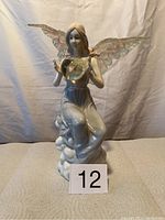 Front view of ceramic angel figurine holding small snow globe with iridescent wings and sitting on cloud base.