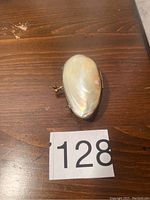 Closed pearl exterior of the antique small change purse on a wooden surface with lot number 128.