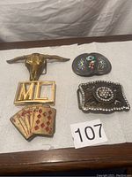 Five belt buckles placed on white towel background with label '107' visible