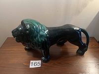 Side angle showing full body of ceramic lion figurine with green and black glaze on wooden surface.