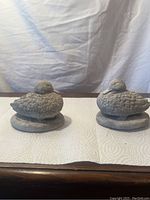 Pair of white stone duck-shaped ornaments as bookends resting on a table with a light fabric background.