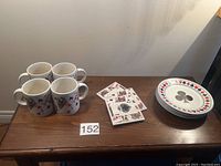 Four coffee mugs, four dessert plates, and three ceramic coasters displayed on a wooden surface against a neutral wall background.