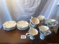 Set of 12 white ceramic coffee cups and matching saucers arranged on table, showing octagonal shapes and Christmas tree decorations on cups.