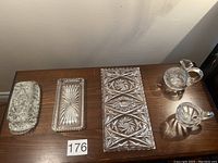 Four crystal items arranged side by side on wooden surface: butter dish with lid, mint tray, elongated serving tray, and two oil and vinegar containers with stoppers and handles