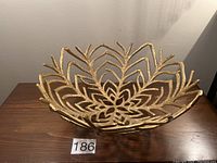 Angled front view of the decorative gold-colored metal bowl showing leaf patterned openwork design