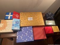 Twelve empty gift boxes varying in size, color, and design arranged on a wooden surface against a wall.