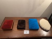Four empty velvet jewellery boxes in burgundy, brown, blue, and cream colors shown from above on a wooden surface.