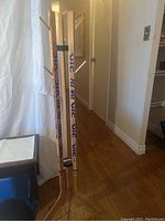 Coat rack constructed from wooden hockey sticks featuring 'Vic' and 'Pee Wee' branding, standing upright, shown from side and front views.