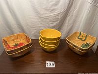 Top view showing four plain round yellow salad bowls stacked and six square yellow salad bowls with vegetable patterns stacked separately on a wooden surface.
