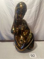 Front view of bronze painted ceramic sculpture showing stylized mother cradling child