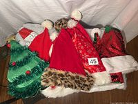 Top view of all ten Santa hats spread on a surface showing designs including green Christmas tree shaped and various red hats with sequins, faux fur pom-poms, and leopard trim.